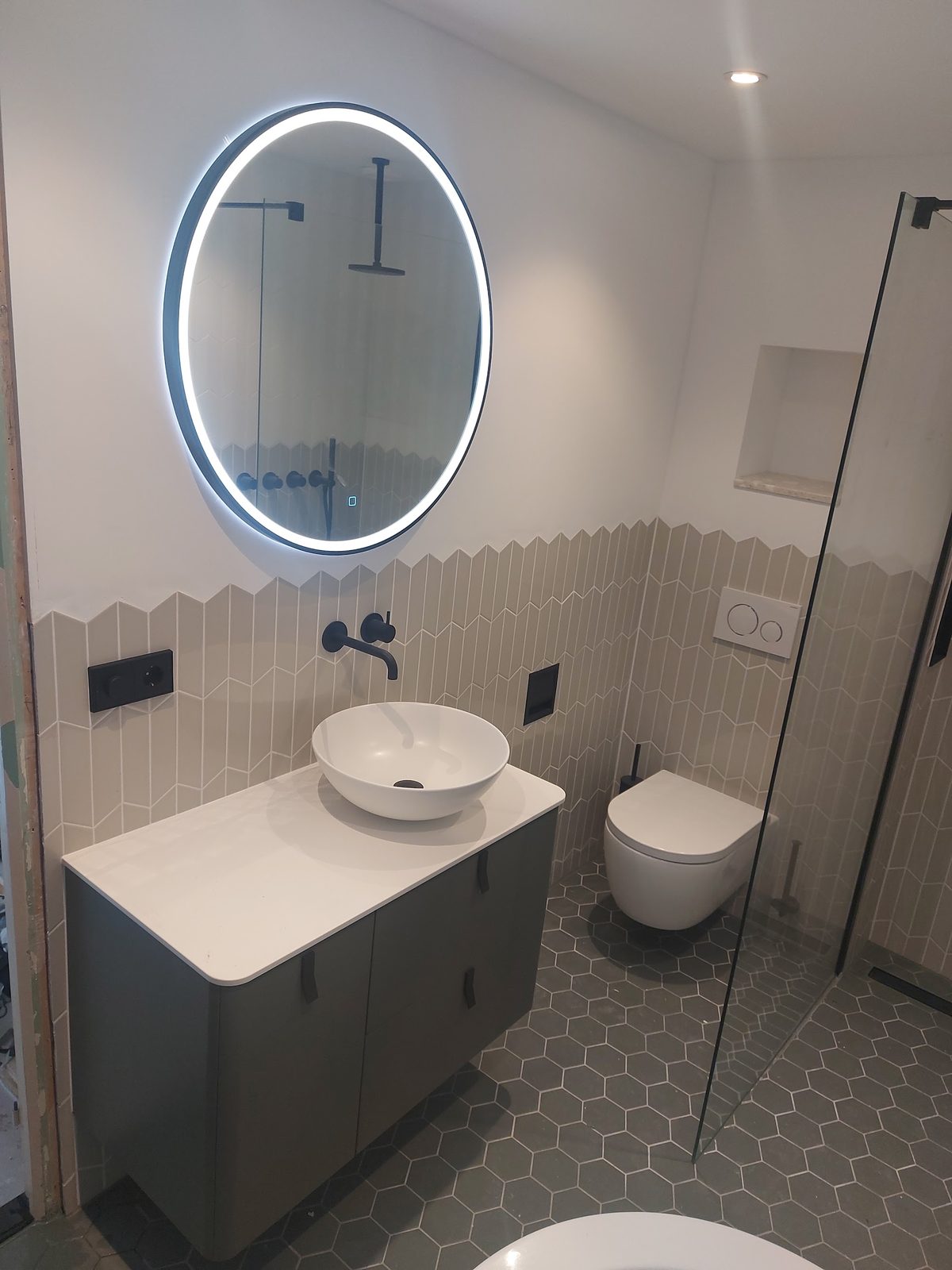 Toiletruimte met zwevend toilet, ronde verlichte spiegel en zeshoekige vloertegels