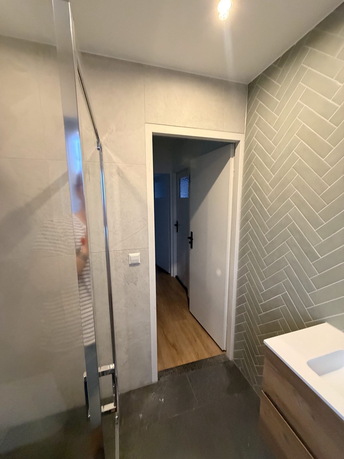 Kleine badkamer met visgraattegels op de wand en een glazen douchewand