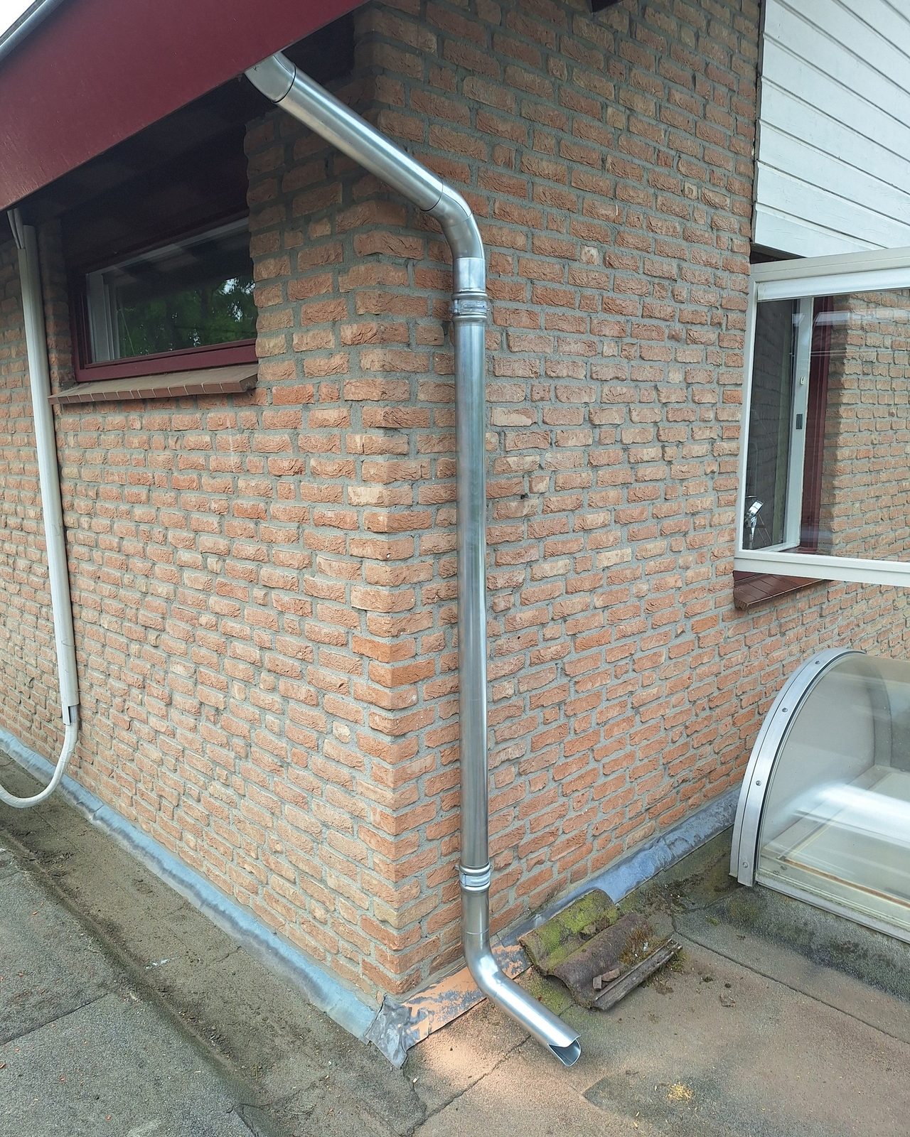Nieuwe zinken regenpijp langs een bakstenen muur